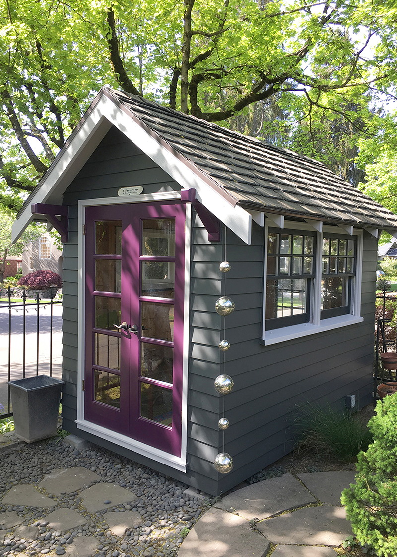 Small detached building with dark grey siding and purple door